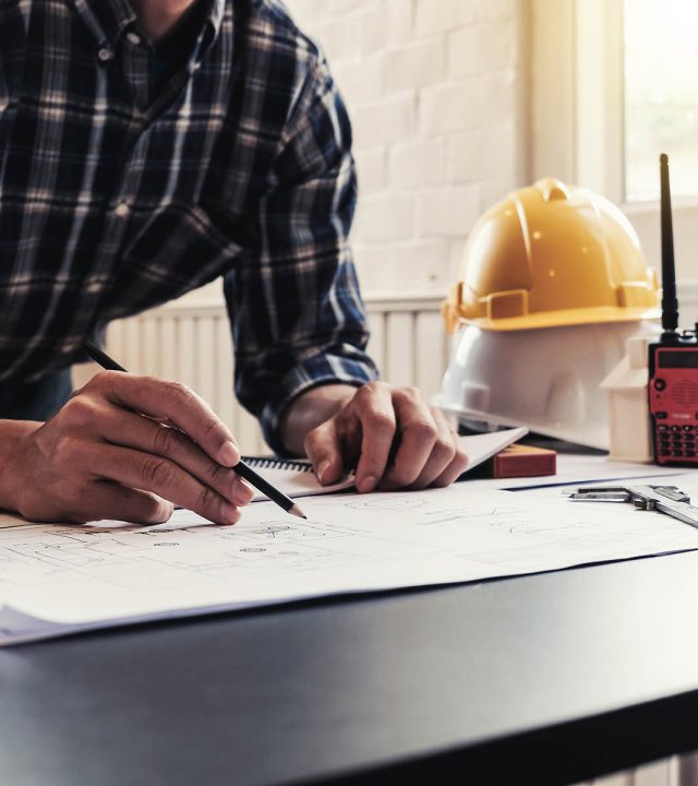 Male architects or engineers write a draft of the construction project on the blueprint.